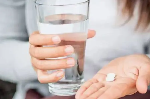 A white acetaminophen tablet beside a glass of water on a plain table, illustrating dosing on an empty stomach for faster absorption.