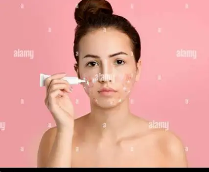 Person gently massaging a thin film of topical cream into their cheek with their fingertips.