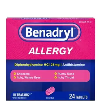 Two small pink tablets resting beside a Benadryl Allergy tablet package on a plain surface
