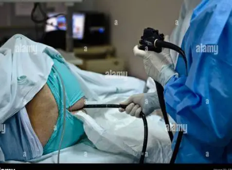 Clinician performing a colonoscopy while an assistant views the colon lining on a bedside monitor