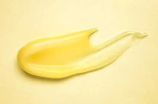 Two small samples of topical skin treatment on a neutral surface, one lighter and one thicker and greasier.
