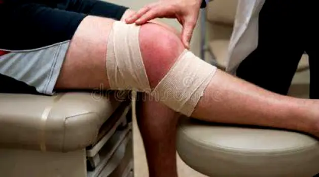 Clinician examining a patient's swollen knee during a physical examination