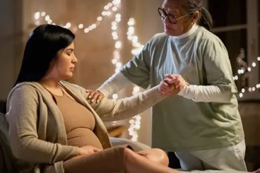 Doula or support person holding the hand of a laboring person and offering a reassuring smile, illustrating the emotional support described in the article.