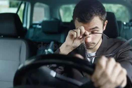 Driver's hands resting loosely on a steering wheel while looking sleepy inside a car