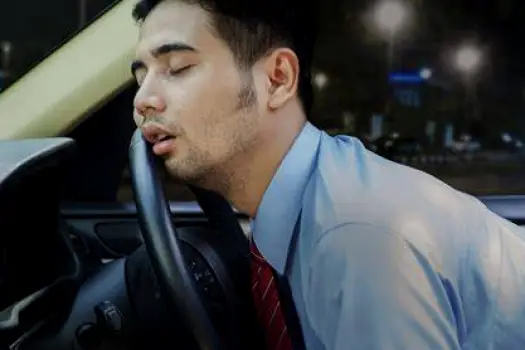 Drowsy person rubbing their eyes behind the steering wheel of a car