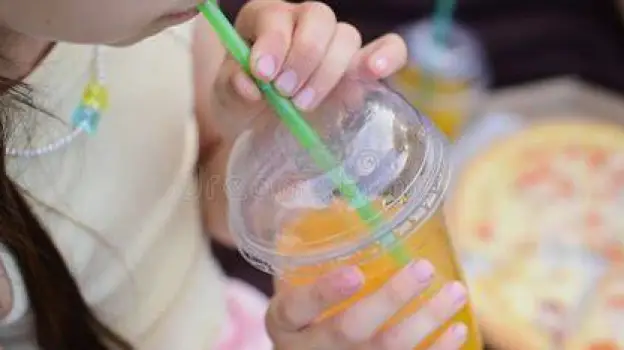 Person eating quickly at a table while drinking a carbonated beverage through a straw.