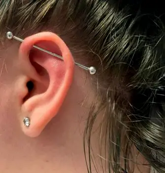 Close-up of an industrial ear piercing with a single metal bar connecting two punctures through the upper ear cartilage