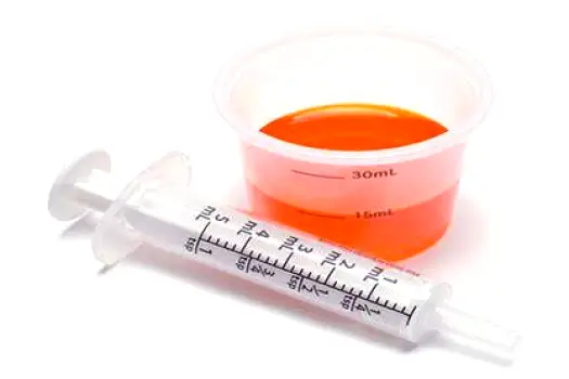 Person measuring a dose of liquid medicine with the dosing cup supplied with the bottle