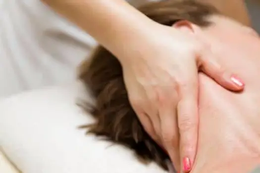 Therapist applying focused pressure to the neck and shoulders of a client lying on a massage table