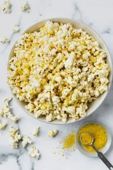 Pale yellow nutritional yeast flakes sprinkled over a bowl of freshly popped popcorn