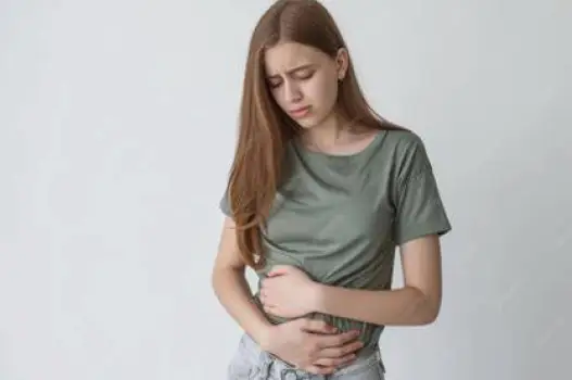 Person sitting at a table with one hand resting on a visibly uncomfortable abdomen, showing tightness and fullness after eating