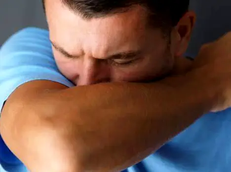 Person sneezing forcefully into their bent elbow