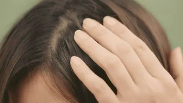 A person gently pressing their fingers against a specific spot on their scalp with a slightly pained expression.