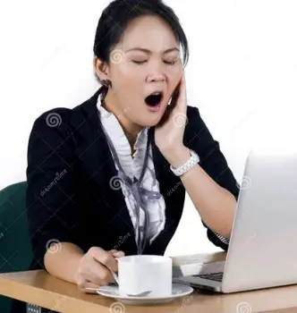 A person seated at a desk covering their mouth while yawning