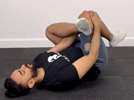 Person lying on back with one ankle crossed over opposite knee pulling uncrossed thigh toward chest