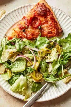 A plate with a pizza slice, a side salad, and a fruit side