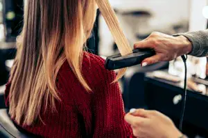 Hair stylist using a flat iron on a client's hair during a chemical smoothing treatment