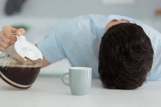 A person yawning while holding a cup of coffee