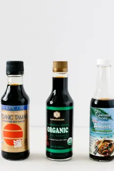 Three bottles on a shelf: traditional tamari, gluten-free soy sauce made with rice, and coconut aminos, showing different gluten-free soy sauce alternatives.
