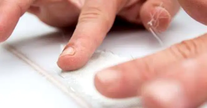 A small strip of adhesive tape being applied to a visible fiber on skin