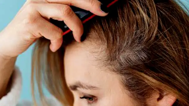 Person wincing slightly while gently combing their hair close to the scalp