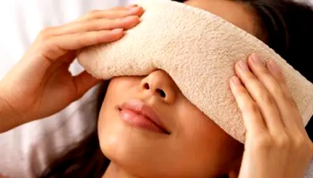 Close-up of a person with their eye closed while a warm, damp cloth is gently placed over the affected eyelid.