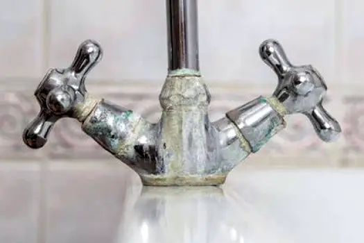 White mineral scale buildup on a metal bathroom faucet from hard water exposure